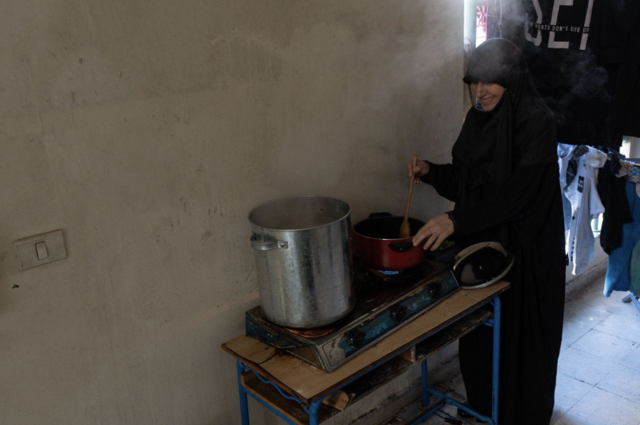 A woman stirs food in a pot against a concrete wall.