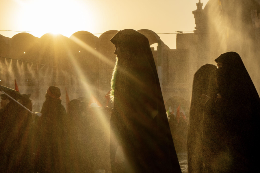 Mourners in black hijabs are backlit by a bright sun.